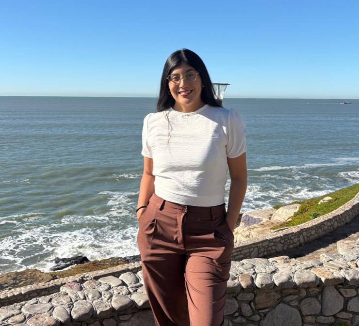 Andrea Garzon sonríe frente al mar, apoyada en una baranda de piedra.