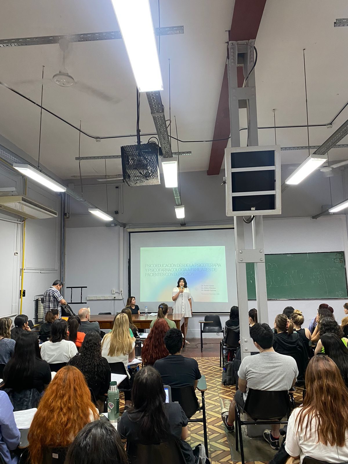 Andrea Garzon expone frente a un aula llena; en la pantalla se lee el título de la presentación.