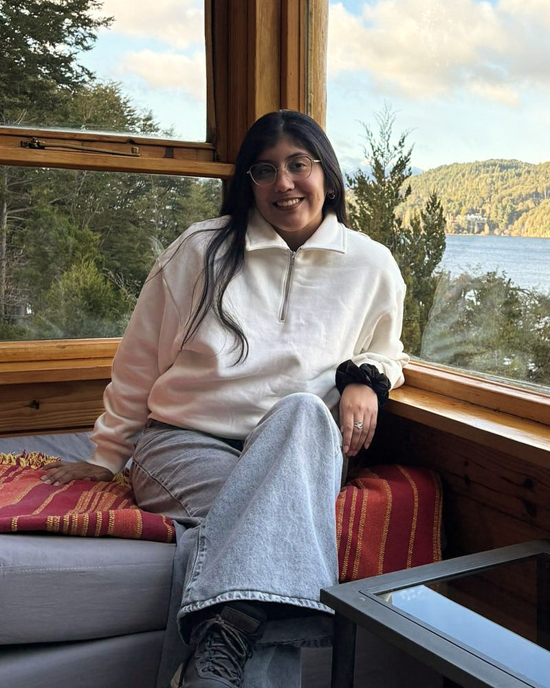 Andrea Garzon sonríe sentada junto a una ventana, con un lago y montañas de fondo.